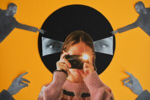 Foto-Collage auf gelbem Untergrund. In der Mitte eine Person, die eine Kamera mit Blitzlicht vor ihr Gesicht hält. Hinter der Person befindet sich ein schwarzer Kreis, in dem rechts und links ein geöffnetes Auge zu sehen ist. An den vier Ecken des Bildes streckt sich ein junger Mann in Richtung der Augen aus.