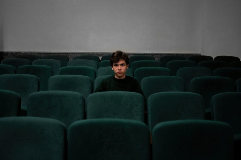 Ein leerer Kinosaal mit dunkelgrünen Sitzen, in der Mitte des Bildes sitzt ein Junge im schwarzen Pullover