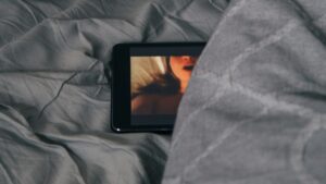 Ein halb verdecktes Tablet unter einer grauen Decke, auf dem vermutlich ein Porno läuft