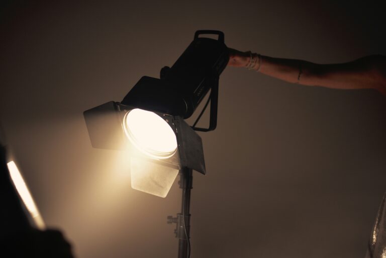 Eine Fotolampe die gelbes warmes Licht nach links unten strahlt, gehalten von dem Arm einer Person auf der rechten Seite