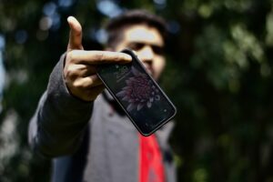 Eine Person hält ein Handy in Richtung Kamera. Die Person ist im Hintergrund unscharf.