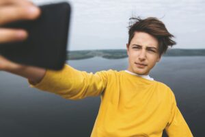 Ein Jugendlicher macht ein Selfie vor einem Hintergrund, der einen großen See oder das Meer zeigt