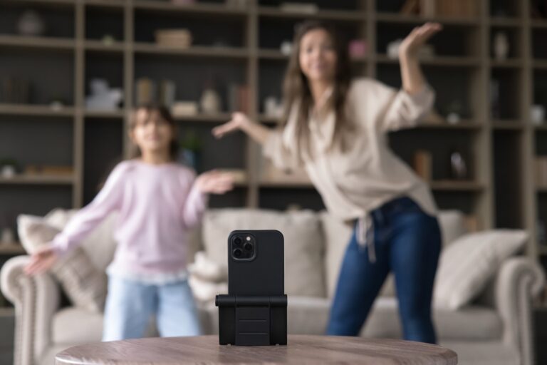 Zwei Mädchen performen im unscharfen Hintergrund vor einem Handy, das im Vordergrund steht