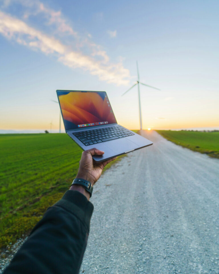 Arm hält einen Laptop in die Luft in Richtung eines Windrades