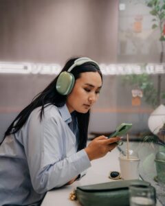 Junge Frau hat Kopfhörer auf und schaut auf ihr Handy