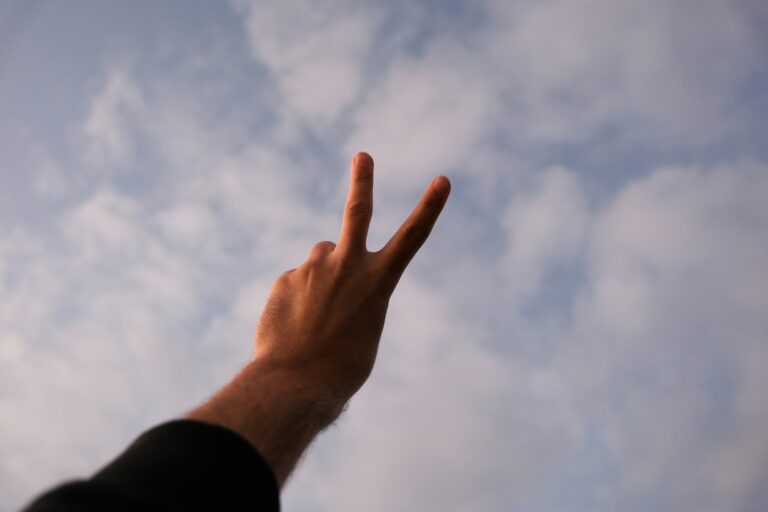 Hand die das Peace Symbol macht vor einem wolkigen Himmel.