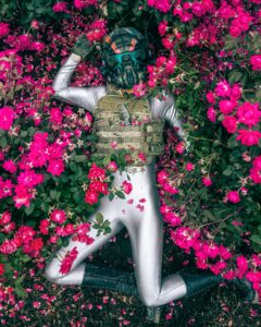 Eine bewaffnete Person im militärischen Kampfanzug, die in einem rosa Blumenfeld liegt