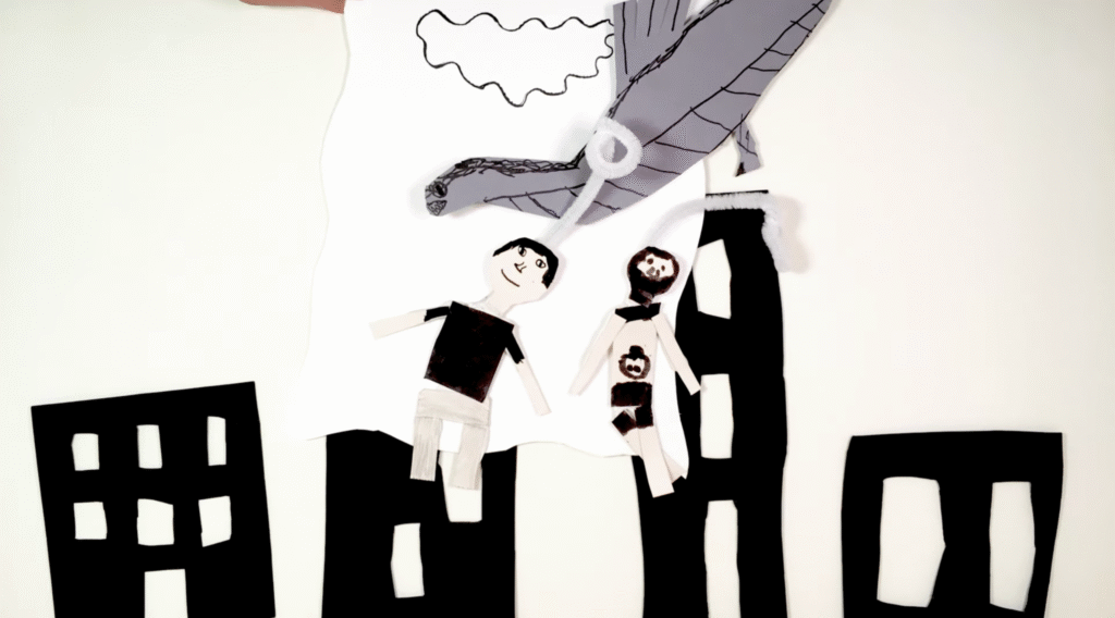 Aus Pappe gebastelte Stadt. Ein Ungeheuer schwebt über zwei Menschen.