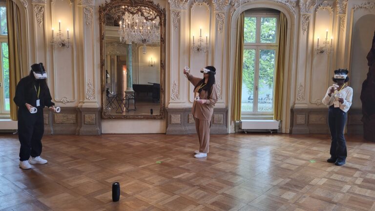 Drei Personen mit VR-Brillen stehen in einem pompösen Raum.