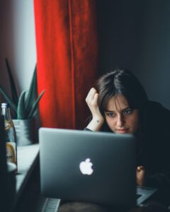 Eine junge Frau sitzt vor einem Laptop und starrt auf den Bildschirm.