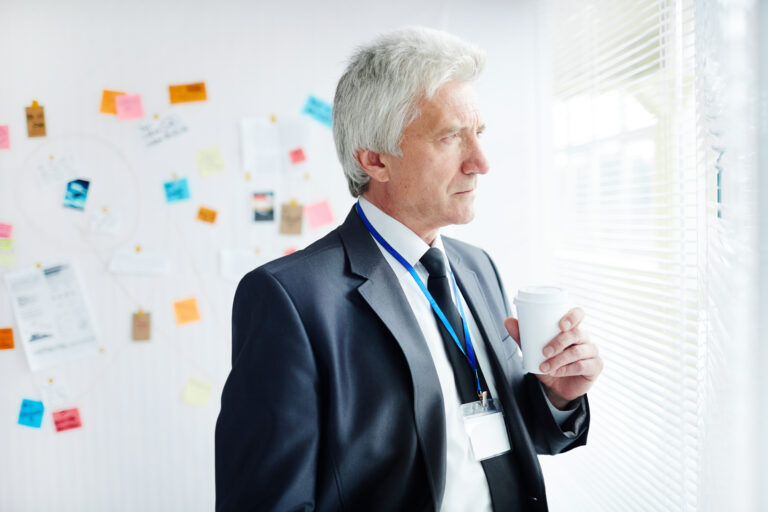 Alter weißer Mann im Büro schaut kritisch aus dem Fenster