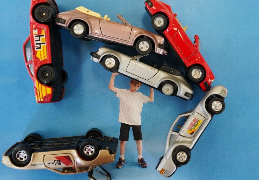 Ein kleiner Junge, der Spielzeugautos &uuml;ber seinen Kopf stimmt