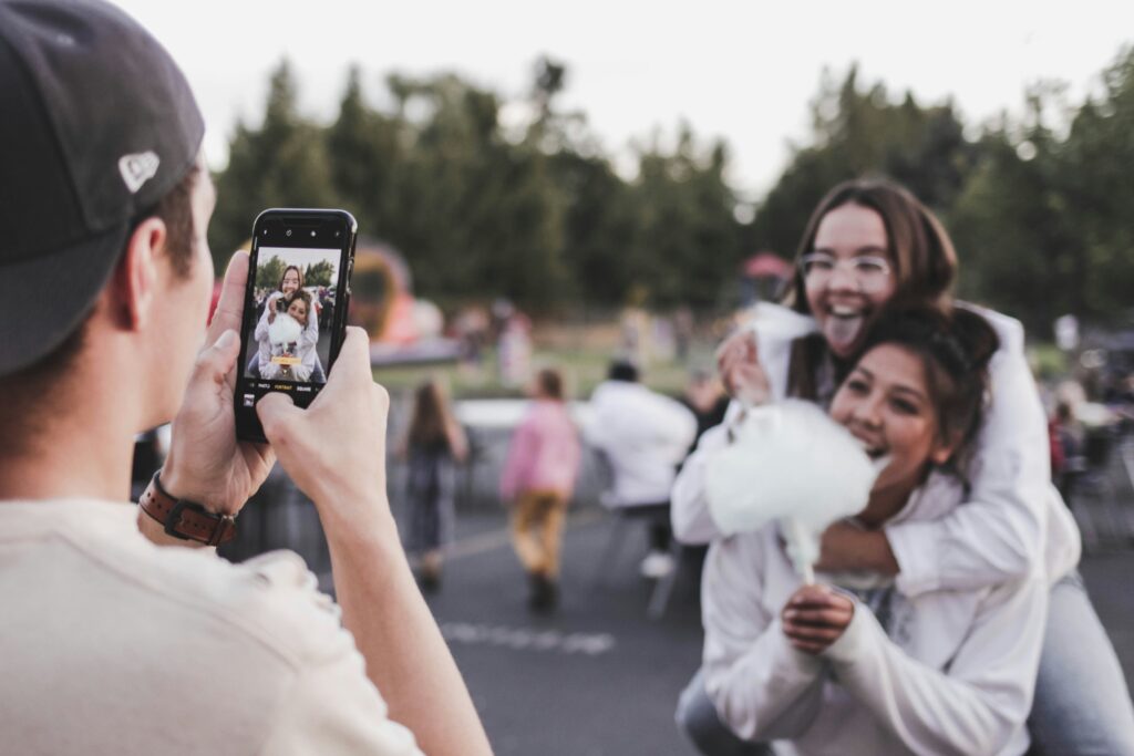 Ein Mann fotografiert mit seinem Handy zwei junge Frauen, die von Zuckerwatte abbeißen.