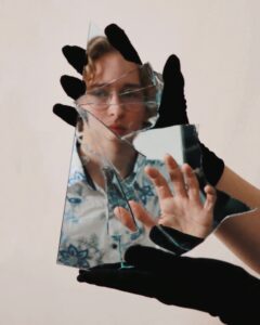 Ein zersplittertes Stück Spiegel, in dem Mann das Gesicht einer jungen Person erkennt