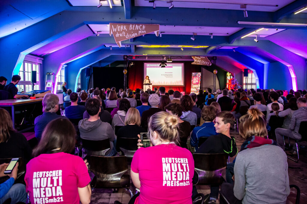 Publikum, dass einer Frau auf einer Bühne zuhört