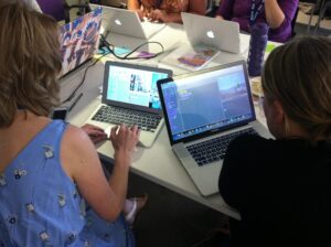 Menschen sitzen an einem Tisch mit Laptops und arbeiten/produzieren etwas