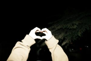 Zwei Hände formen ein Herz, die Hände sind mit einem Fotoblitz angestrahlt