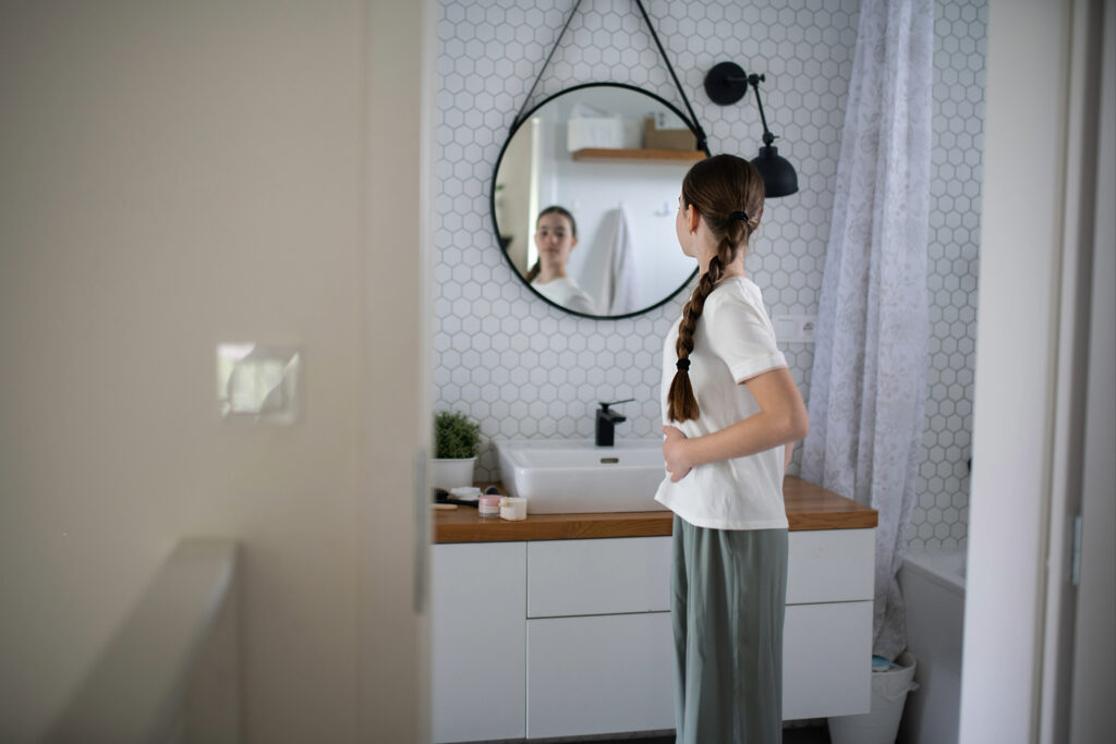 Ein junges Mädchen, dass sich, vor allem ihren Körper, im Badezimmer Spiegel betrachtet und ihre Hände an ihren Bauch hält