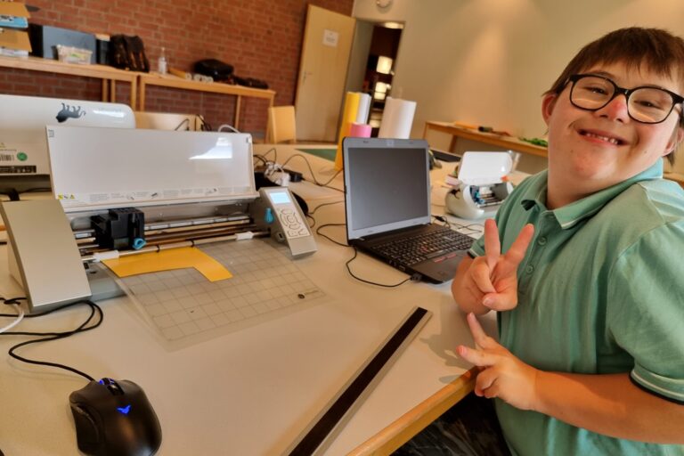 Person sitzt an Werktisch und erstellt einen Aufkleber.