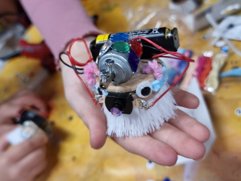 Ein bunter gebastelter "Bürstenroboter" mit Wackelaugen und Glitzersteinen verziert.